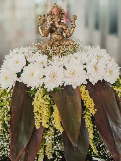A Ganesh idol placed on a beautiful arrangement of white chrysanthemums and dark leaves, a tradition we follow to bring auspicious beginnings to every event.