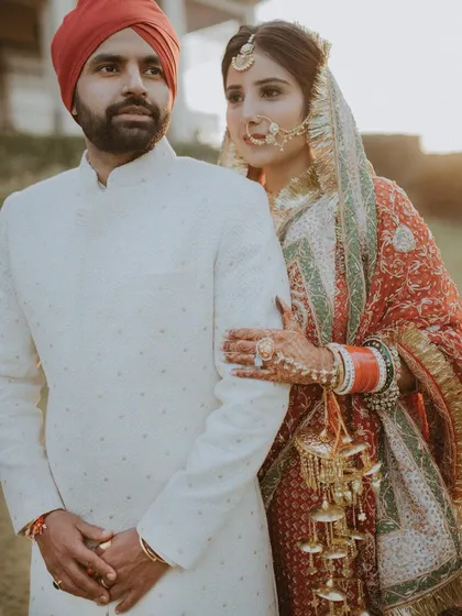 A classic portrait of a Sikh couple, the bride holding the groom's arm, showcasing their traditional attire.