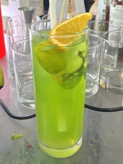 A bright green cocktail garnished with fresh mint and an orange slice. The color contrast is visually stunning.