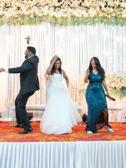 The bride and groom on stage with their wedding party and emcee, sharing a fun, choreographed moment with their guests.