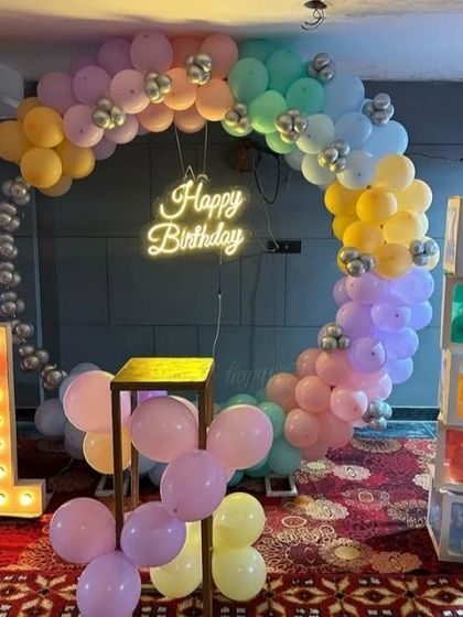 A pastel rainbow balloon ring for a first birthday. This decoration includes a light-up number '1', a neon sign, and custom letter blocks.