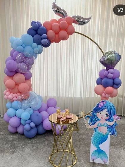A beautiful mermaid-themed setup with a balloon arch in ocean colors, a mermaid tail, and a character cutout.