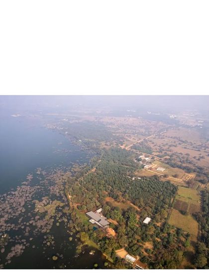 A wide aerial shot capturing the entire 600-meter lake edge of the property. The house is a small, respectful intervention in a magnificent natural setting.