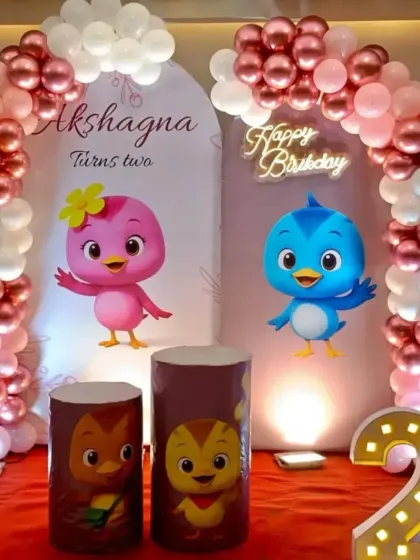 A cute bird-themed party for a second birthday, featuring character cutouts on pedestals and balloon arches in pink, rose gold, and white.