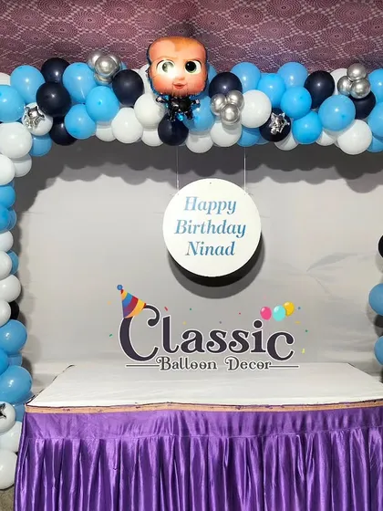 A Boss Baby themed cake table setup for a first birthday. The balloon arch in blue, black, and silver frames the table perfectly.