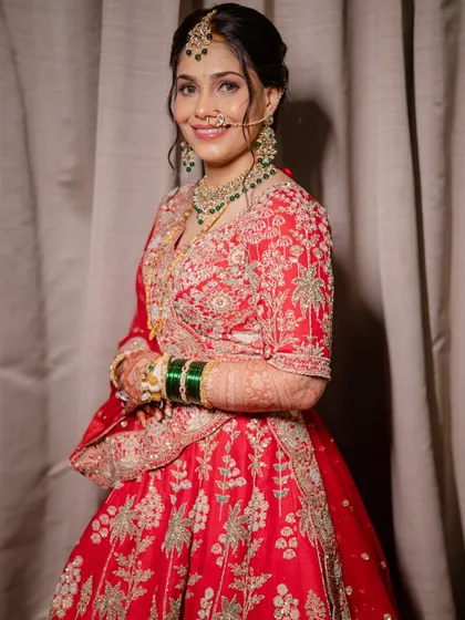 A full portrait of the bride in her stunning red lehenga. The outfit is draped perfectly, and her hair is styled in an elegant updo to complete the royal look.