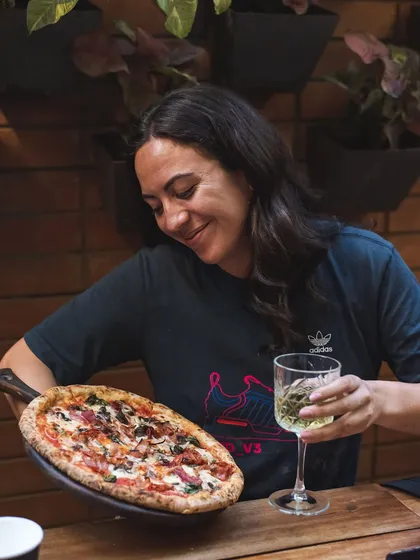 A customer admiring her freshly made pizza, paired with a glass of white wine. Happiness is having pizza.