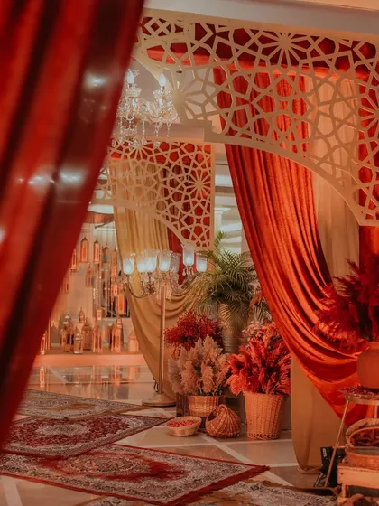 A view through crimson velvet drapes into a space decorated with jaali-cutout arches and rich textiles, showcasing our use of layering to create depth and intrigue.