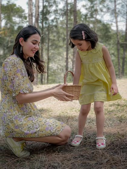 A mother and daughter share a moment with a small wicker basket in a beautiful forest setting.