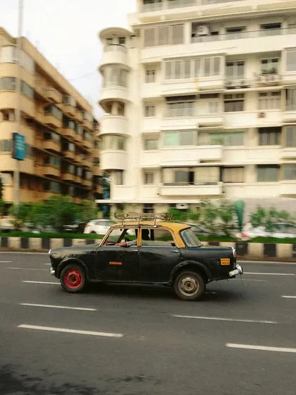 A panning shot of a Kaali-Peeli taxi in motion along Marine Drive. The motion blur in the background conveys speed and energy, capturing the taxi as a dynamic part of the city's landscape.