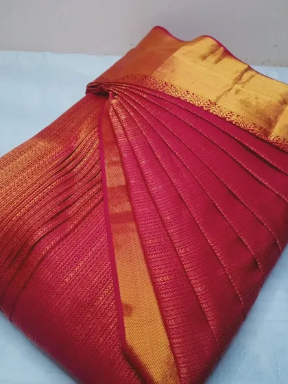 A rich red silk saree with a gold border, pleated and box-folded.