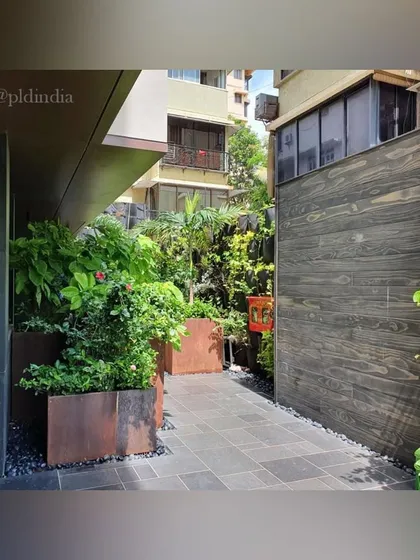 This narrow space between buildings becomes a charming garden path. The contrast between the dark wood-paneled wall and the vibrant green plants in corten steel planters is visually striking.