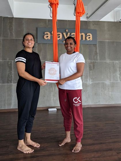 An instructor presents a certificate to a newly qualified aerial yoga teacher. We are so proud of our graduates.