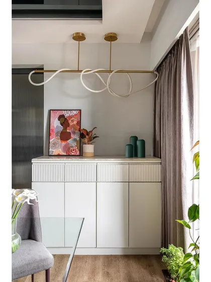 This elegant crockery unit features clean white lines, fluted detailing, and a modern sculptural light fixture. It provides ample storage while serving as a beautiful decorative element in the dining area.