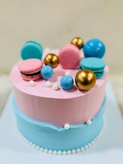 A chic heart-shaped cake in pink and blue, elegantly decorated with colorful macarons and pearl details.