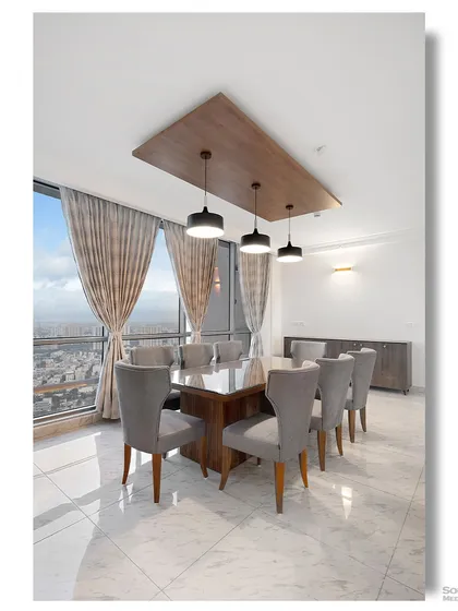 A bright dining area with a view of the city skyline. The simple wooden table and grey upholstered chairs are illuminated by modern pendant lights, creating an elegant space for meals with a view.