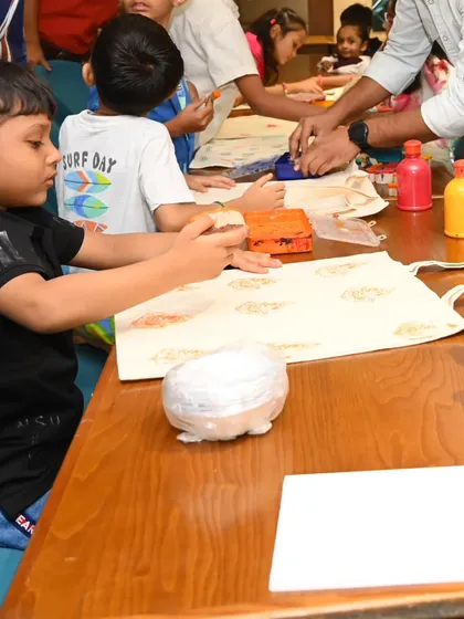 Children are gathered around a table filled with paints and art supplies, focused on their tote bag projects. We set up everything needed for the workshop, creating an organized yet playful environment for creativity to flourish.