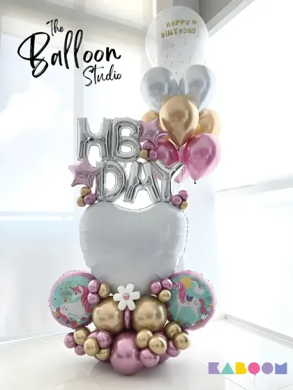 A magical unicorn-themed "HB DAY" balloon arrangement, combining pastel pinks, purples, and golds with unicorn and heart-shaped foil balloons.