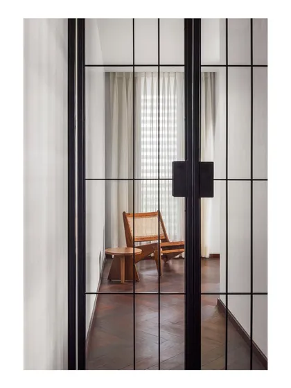 Looking through the full-height pivot metal doors into the master suite lounge. The caned armchair and wooden side table I designed create a warm, welcoming vignette that draws you into the space.