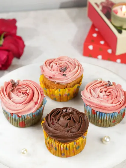 A plate of beautifully decorated Valentine's cupcakes with rose-like frosting, styled with pearls and a gift box.