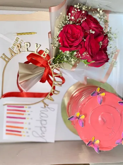 Here’s a look inside our classic birthday hamper box. This one includes a beautiful pink jar cake with butterfly details, a fresh bouquet of red roses, a 'Happy Birthday' tiara, candles, and a card.