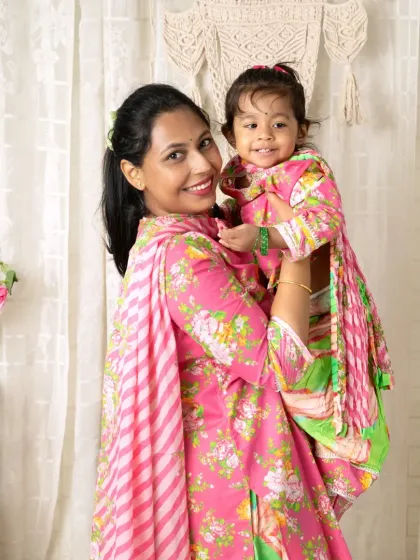 A mother holds her daughter in her arms, both dressed in beautiful matching floral outfits.