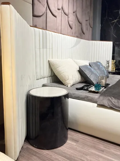 This bed features a tall, winged headboard with vertical channel tufting in a cream-colored fabric. The design creates a grand and luxurious focal point, complemented by a dark, textured wall panel.