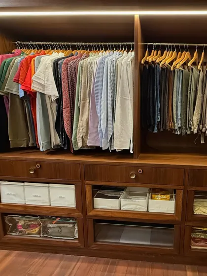 The "his" side of the closet, with neatly hung shirts and trousers above drawers and bins for folded items.