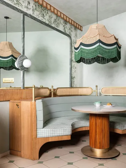 For this commercial project, we designed a space that feels nostalgic but never dated. The custom curved booth seating, upholstered in sage green and gingham, is paired with a fluted-base table and a statement scalloped pendant light, showcasing our attention to bespoke detail.