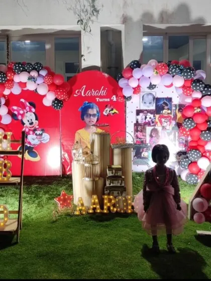 An outdoor Minnie Mouse themed party setup on an artificial grass lawn, with character cutouts and marquee letters.