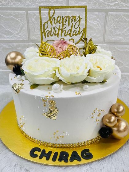 A chic white birthday cake topped with pristine white roses, gold accents, and a miniature golden carriage for a touch of fairytale magic.
