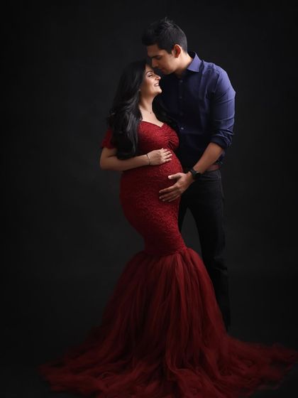 A bold and passionate maternity portrait. The deep red lace gown against a dark backdrop creates a dramatic and powerful image celebrating the strength of motherhood.