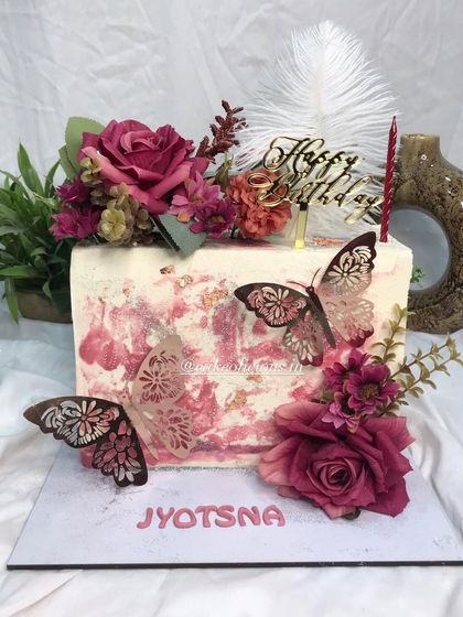 My first rectangular top-forward cake, and it came out so perfectly. This floral beauty features a white chocolate ganache with a pink textured effect, adorned with deep red roses, elegant butterflies, and a feather. The flavor inside is classic pineapple.