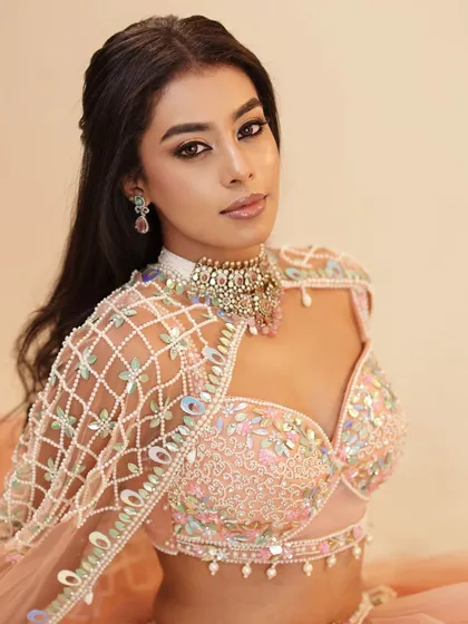 A modern and chic look in a pastel peach lehenga with a unique cape. The makeup is soft and neutral, letting the intricate outfit shine.