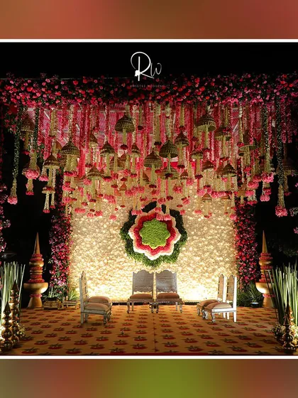 A beautiful stage for a traditional ceremony, with a backdrop of white flowers and a floral 'rangoli' design. The hanging floral tassels add a unique touch.