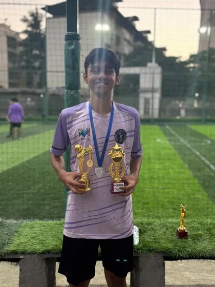 A proud U-15 player showcasing his team and individual trophies after a successful tournament.