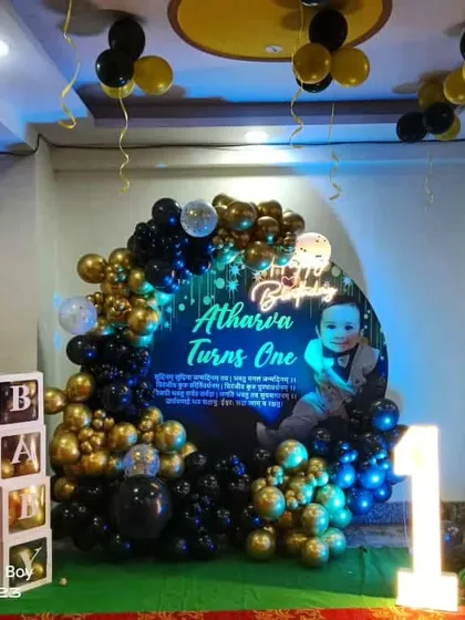 A stylish first birthday setup with a 'Boss Baby' theme. The decoration features a personalized circular backdrop, a black and gold balloon arch, character cutouts, and a light-up marquee number '1'.