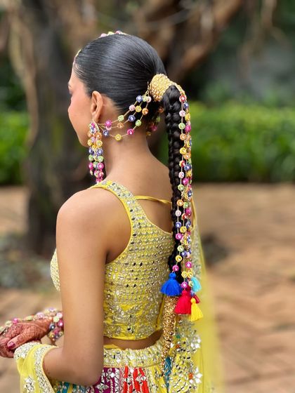 A full view of the Haldi look, showing how the long, accessorized braid complements the bride's vibrant yellow lehenga. This hairstyle is a statement piece in itself.
