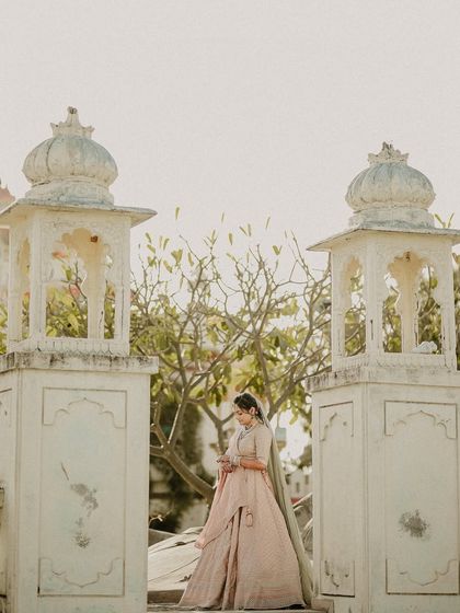 An ethereal solo portrait of the bride standing between two traditional gateposts. Her elegant pose and the soft light create a timeless and graceful image.