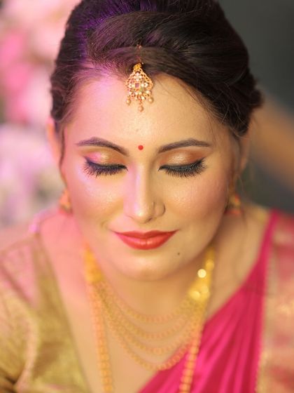 A close-up of a bride's Muhurtham makeup. The focus is on flawless skin with a golden glow, classic winged eyeliner, and a bold red lip. This timeless combination ensures the bride looks stunning for her main ceremony.