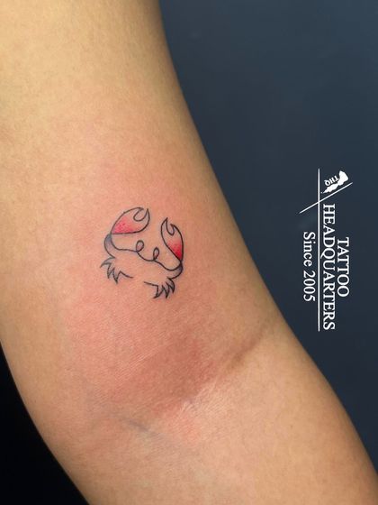 A small, minimalist crab tattoo with red claws, representing the Cancer zodiac sign.