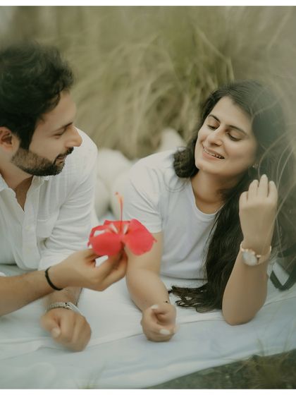 A sweet and romantic moment during a picnic-style shoot. The groom offers a flower to his bride, capturing a simple gesture of love in a relaxed, outdoor setting.