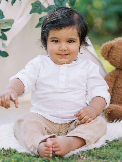 A sweet portrait of the birthday boy sitting in a teepee, looking happy and content during his outdoor celebration.