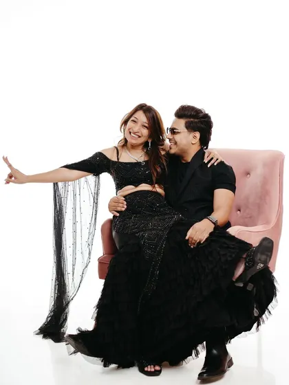 A playful and chic studio shot featuring a pink chair as a prop. The woman sits on her partner's lap, smiling at the camera, showcasing how simple props can add personality to a minimalist pre-wedding photo session.