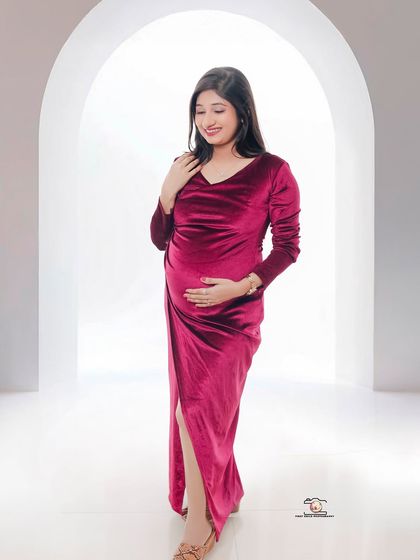 A gentle and classic maternity pose. The mother-to-be cradles her bump with both hands, her soft smile and the elegant magenta gown creating a timeless portrait.