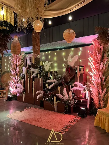 A cozy and stylish photo booth area featuring a wall of dried palm leaves and pampas grass, a modern neon sign, and a comfortable rug.