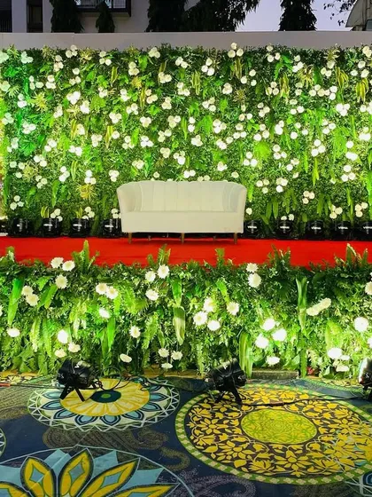 A lush green stage created for a birthday event. The backdrop is a dense wall of leaves and white flowers, providing a fresh and elegant setting.