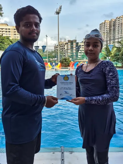 A young female swimmer receives her certificate of achievement from her coach at our pool, marking her successful progression.