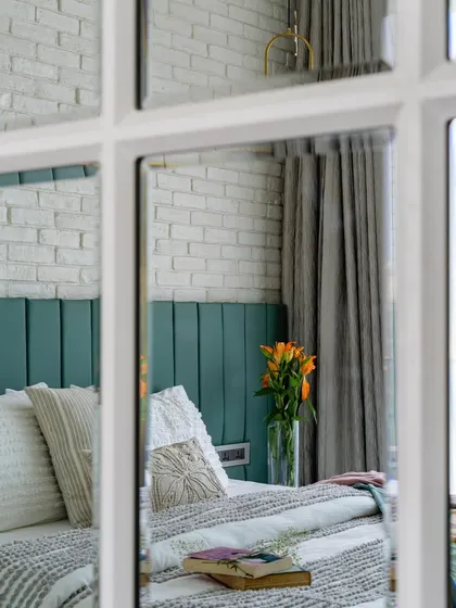 A view through the panes of a mirrored wardrobe in the 'Urban Oasis' bedroom. This shot highlights the green headboard and the layers of texture in the room.