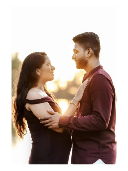 A romantic close-up of an expecting couple gazing into each other's eyes, backlit by the warm glow of the setting sun.